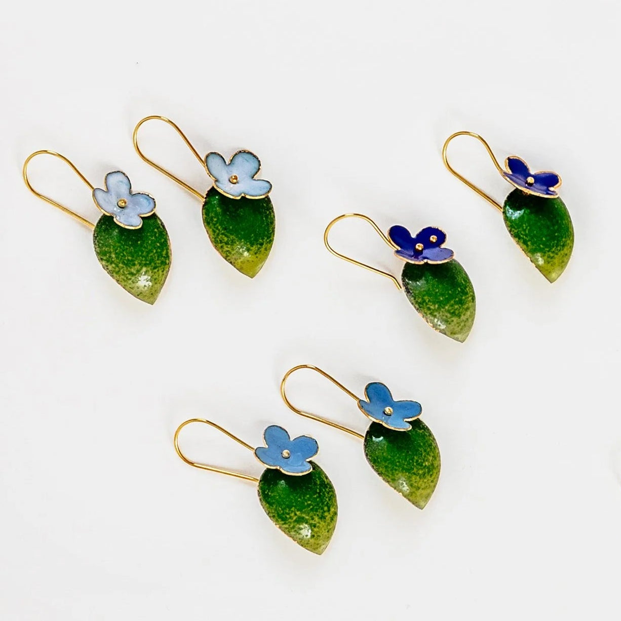 Three pairs of earrings with green leaves and a flower on top.