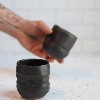 Person holding a textured black ceramic cup on a light surface