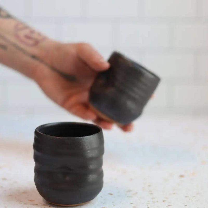 Hand holding a white ceramic cup over another similar cup on a light background
