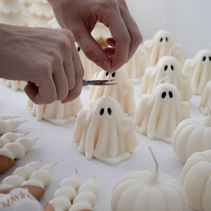 Two ghost-shaped candles with lit wicks on a neutral background