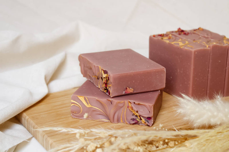 Soap bars with gold designs on a wooden board with dried plants and white fabric.