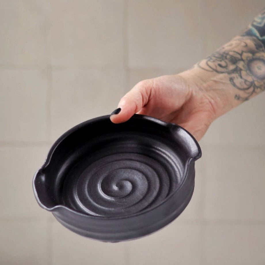Person holding a black cast iron pot with swirling design against a neutral background