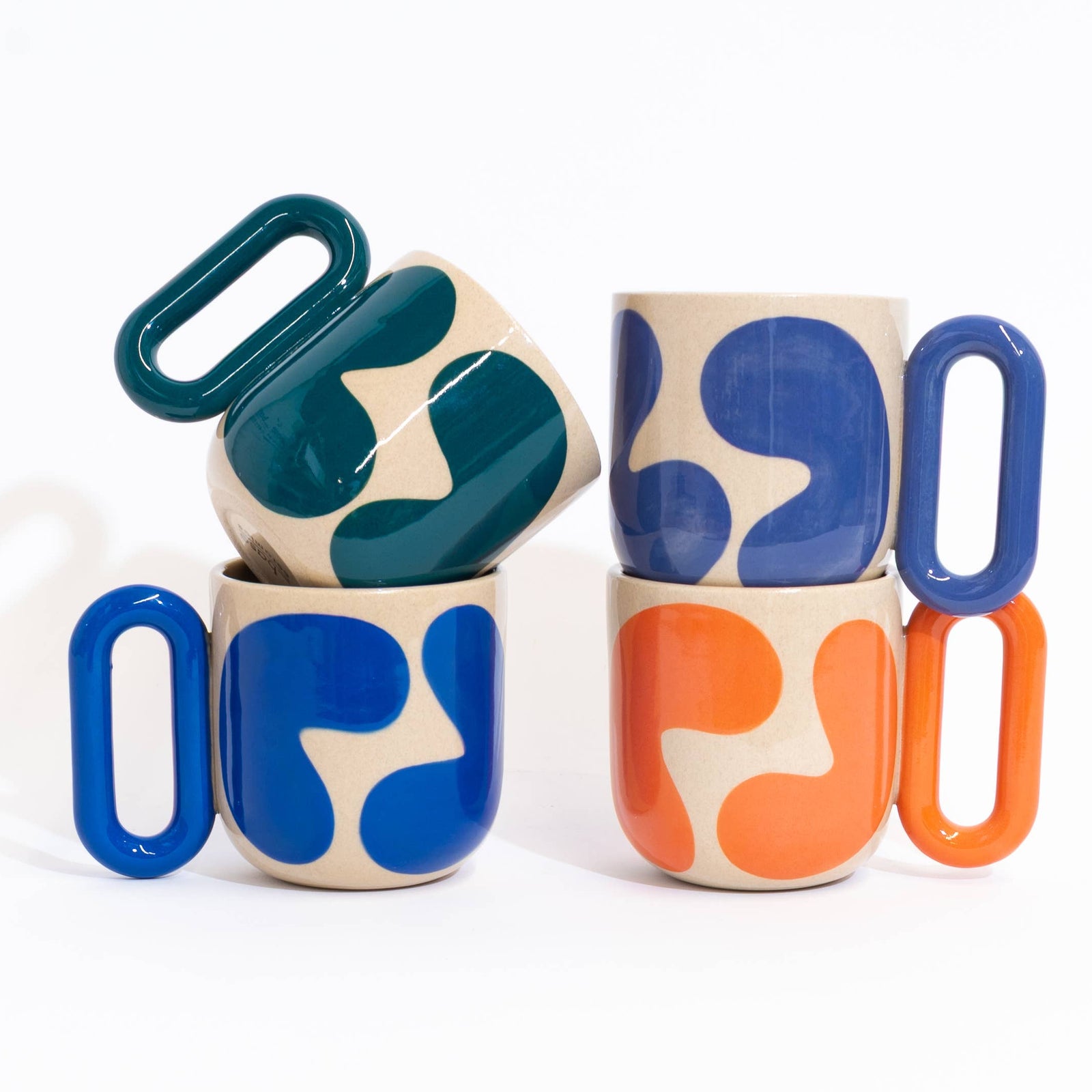 Three ceramic mugs with bold abstract color-blocked patterns in blue, orange, and teal on a cream base, arranged on a clean white background.