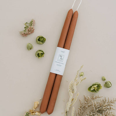 Two terracotta candles with a label on a light background with flowers and plants.
