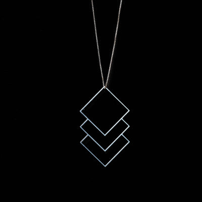 A silver geometric pendant necklace featuring three stacked diamond outlines on a fine chain, set against a solid black background.