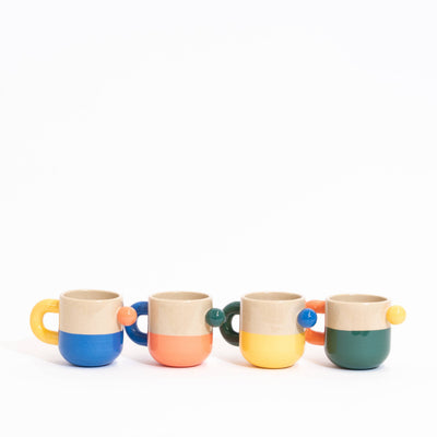 Four small ceramic mugs with half-tone handles, lined up in a row on a white background. Each mug has a beige upper half and a different colored lower half: blue, orange, yellow, and green.