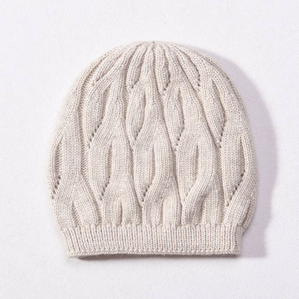 A cream-colored cable-knit beanie hat with a ribbed brim, photographed flat on a light background.