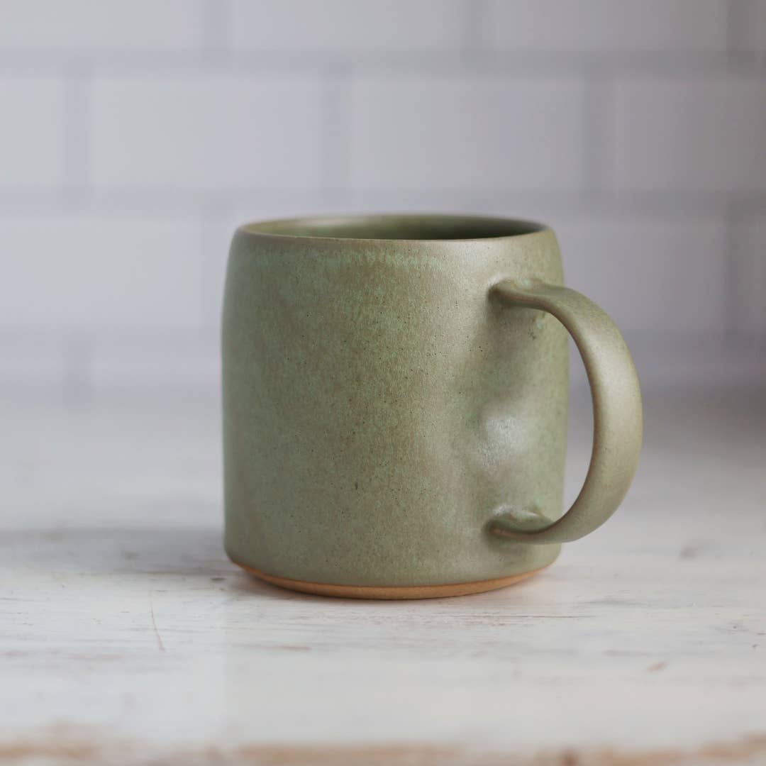 Green ceramic mug on a light wooden surface with a blurred white background