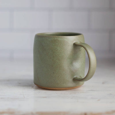 Green ceramic mug on a light wooden surface with a blurred white background