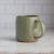 Green ceramic mug on a light wooden surface with a blurred white background