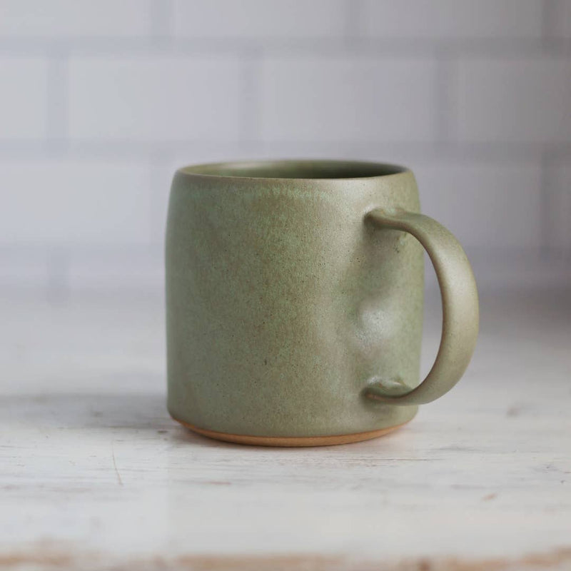 Green ceramic mug on a marble surface with a tiled wall background