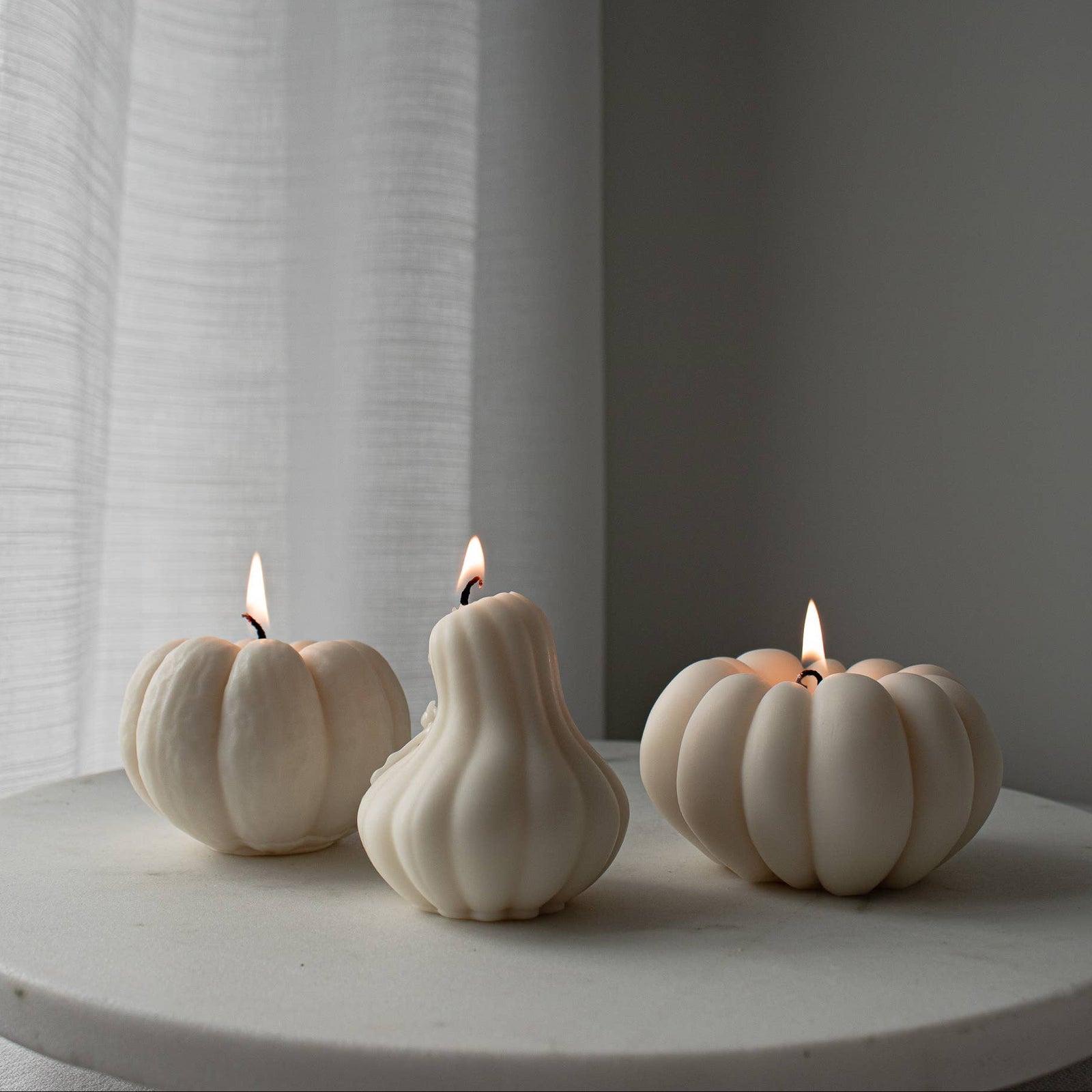 Three white pumpkin-shaped candles on a round surface with a neutral background