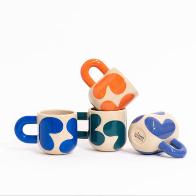 Four small ceramic mugs with abstract organic shapes in blue, green, and orange on a cream base, arranged together on a white background.