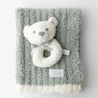Fluffy white teddy bear rattle on a textured green blanket