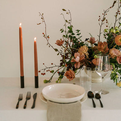 Table setting with candles, flowers, and cutlery on a white surface.