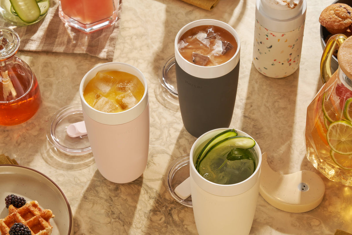Table with various drinks in colorful tumblers and snacks on a wooden surface