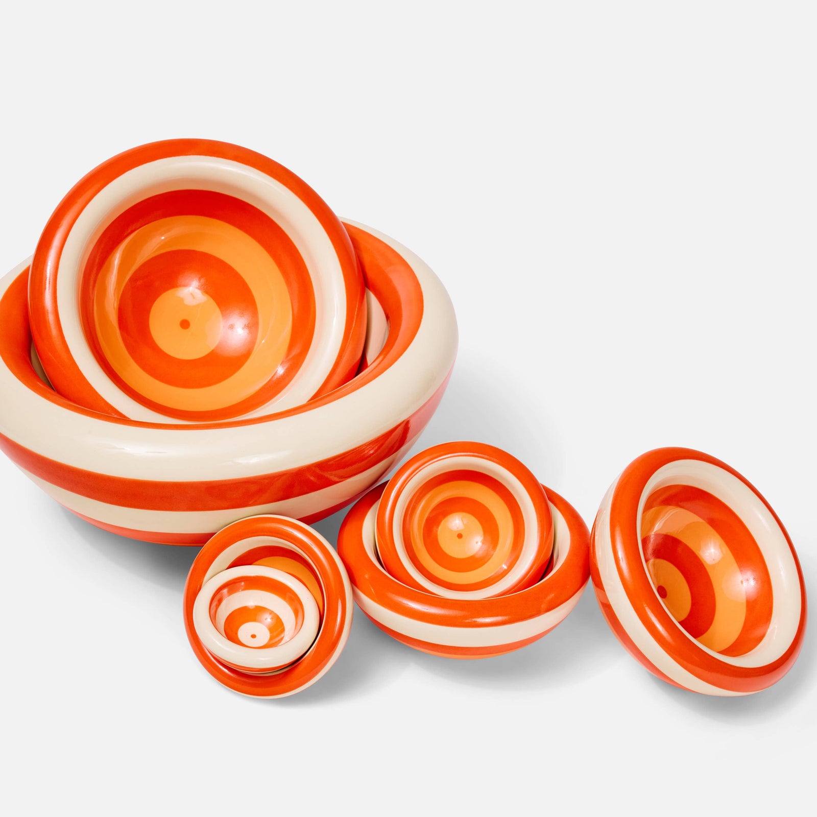 A set of ceramic bowls with concentric orange and cream spiral patterns, arranged on a white background.
